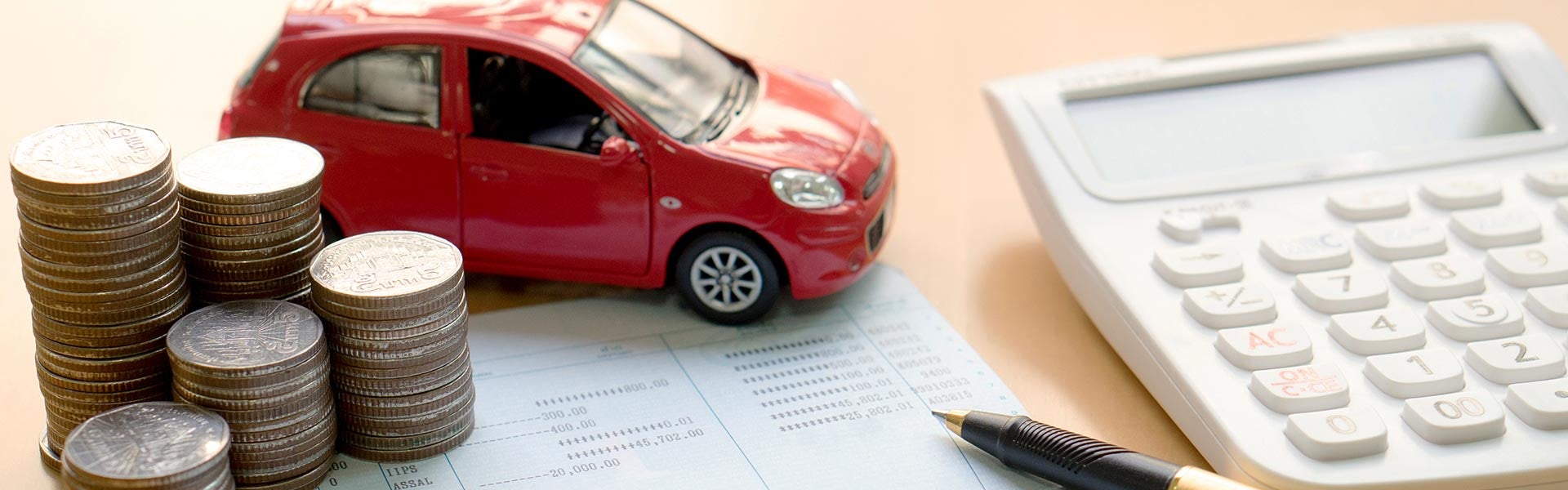 A red miniature toy car resting on financial documents next to stacked coins, a pen, and a white calculator.